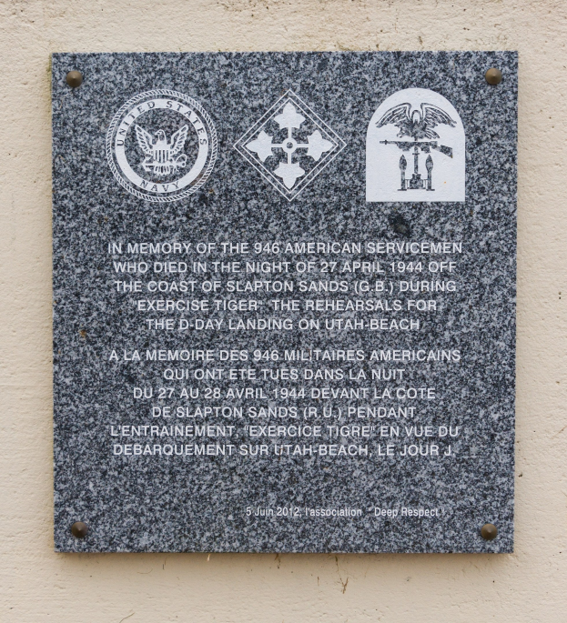 Stone plaque on a building's exterior engraved with "In Memory of the 946 American Servicemen" and logos.
