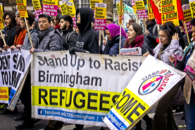 A diverse group of people marching down a street holding protest signs in front of a building with windows.