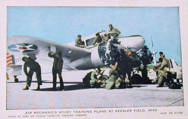 A group of people standing around a training airplane on a runway with a clear blue sky, labeled "Air Mechanics Study Training Plane at Keesler Field, Miss."