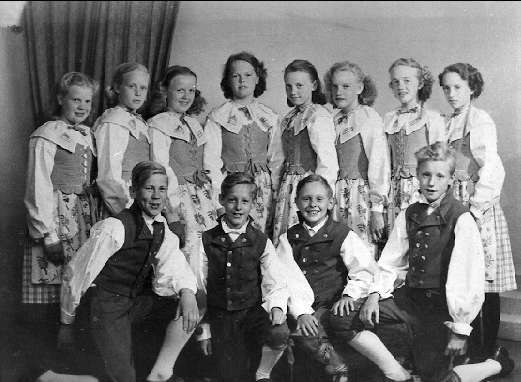 Schwarz-weiß-Foto von Kindern, die vor einem Vorhang posieren, mit dem Text "1930er Kinder-Schule" unten.