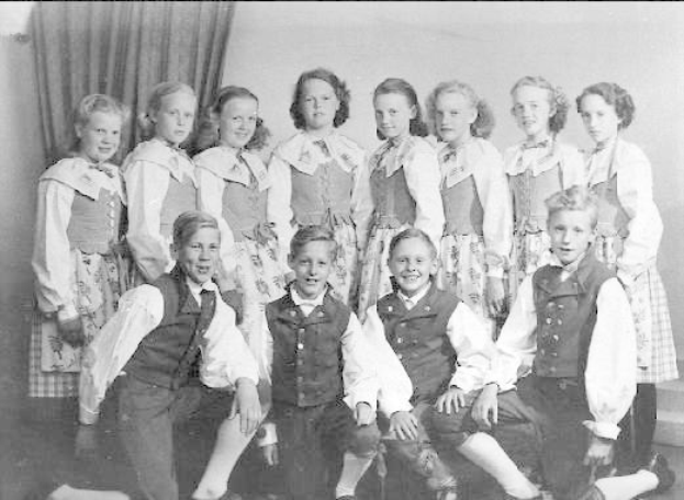 Schwarz-weiß-Foto von Kindern, die vor einem Vorhang posieren, mit dem Text "1930er Kinder-Schule" unten.