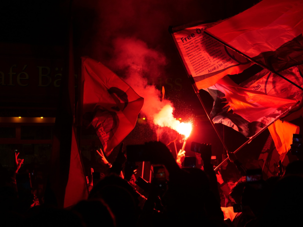 Menschen mit Flaggen und Fackeln vor einem Gebäude mit sichtbarem Text protestieren