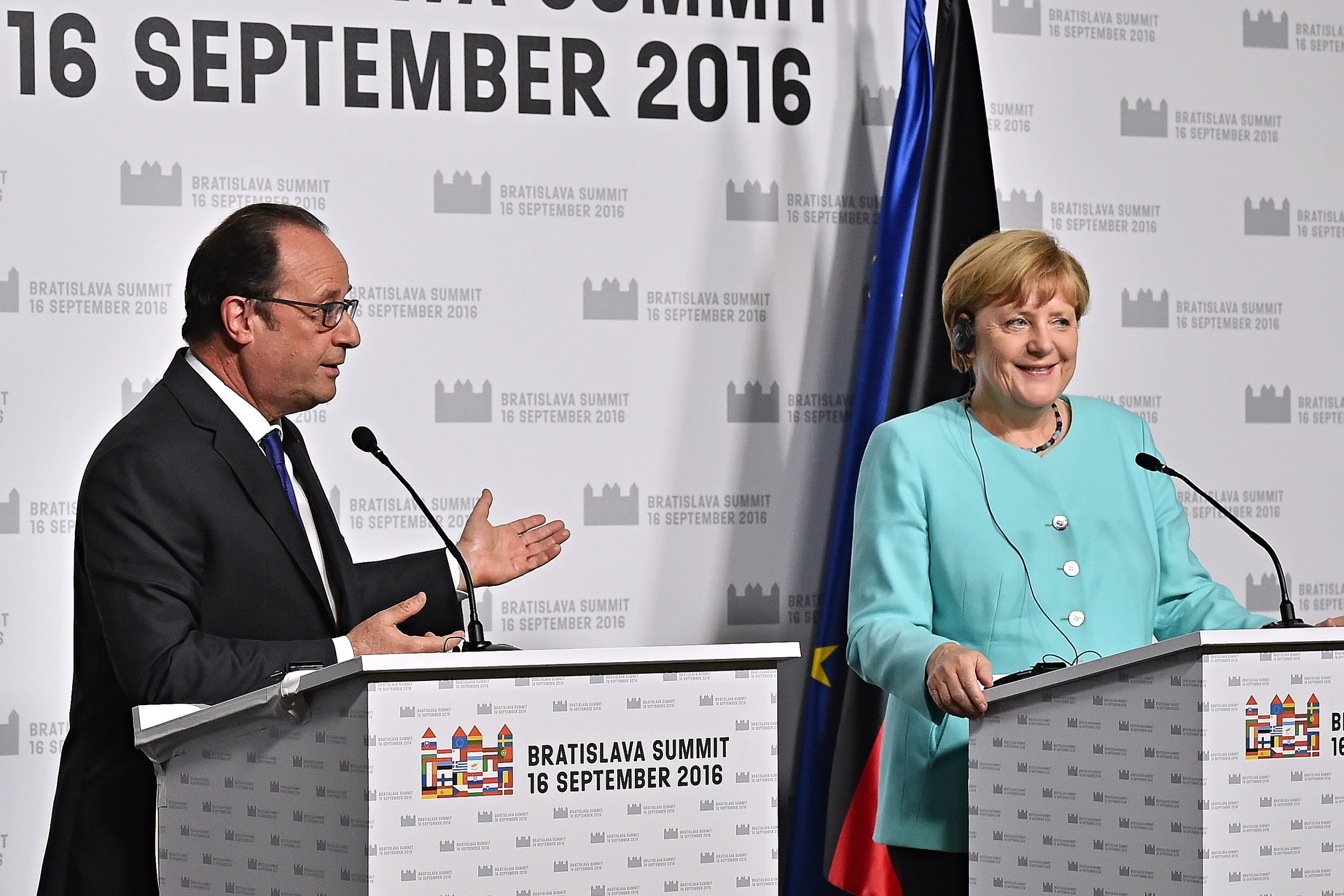 Two smiling leaders, Angela Merkel and Francois Hollande, stand at podiums with microphones in front of a "Bratislava Summit 2016" banner.