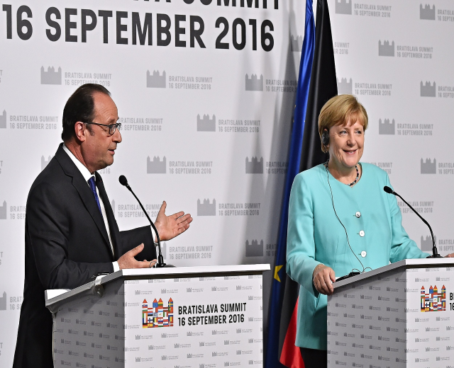 Two smiling leaders, Angela Merkel and Francois Hollande, stand at podiums with microphones in front of a "Bratislava Summit 2016" banner.