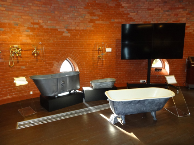 Ein gemütliches Badezimmer mit einer Ziegelwand, einer zentralen Badewanne, an der Wand montierten Hähnen auf der linken Seite und einem an der Wand montierten Fernseher auf der rechten Seite.