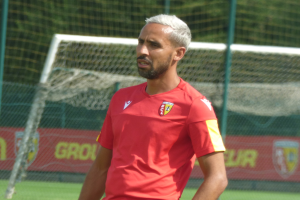 Ein Mann in rotem T-Shirt steht auf einem Fußballfeld und schaut in die Ferne mit einem Netz und einer "Rajasthan FC"-Fahne im Hintergrund.