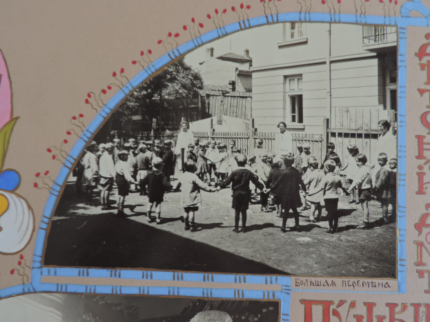 Schwarz-weißes Foto von Kindern, die in einer Straße mit Gebäuden, Bäumen und einem Zaun spielen.