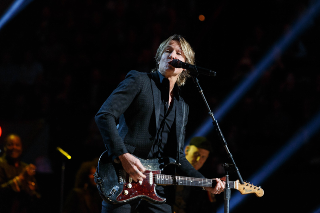 Keith Urban performing on stage at the Joint at Hard Rock Hotel & Casino in Las Vegas, playing guitar with a microphone and band members visible in a dimly lit setting.
