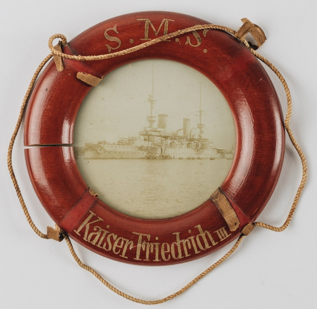 Roter Schwimmwestenaufkleber "USS Kaiser Friedrich III" mit einem Bild eines Schlachtschiffs, an einer weißen Oberfläche mit Seilen befestigt.