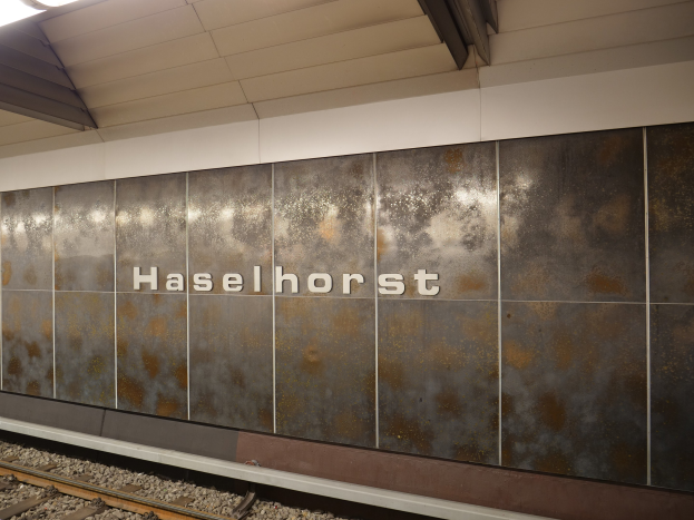Exterior view of a Berlin train station platform with a "Haselhorst" sign illuminated on the wall.