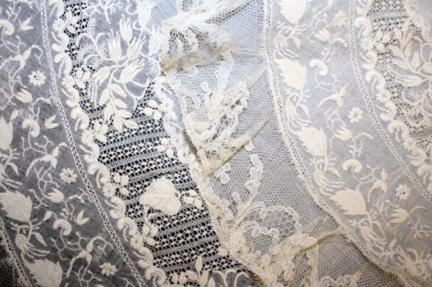 Nahaufnahme eines weißen Hochzeitskleids mit feiner Spitzenverzierung, das zarte Muster und einen leichten, luftigen Stoff zeigt.