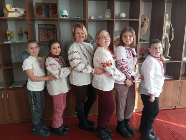 Eine Gruppe von Kindern in traditioneller ukrainischer Kleidung vor einem Bücherregal mit Spielzeug, einem Skelett und anderen Gegenständen.