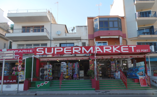 A supermarket at a street corner with buildings in the background, featuring various urban elements like signboards, poles, and plants.