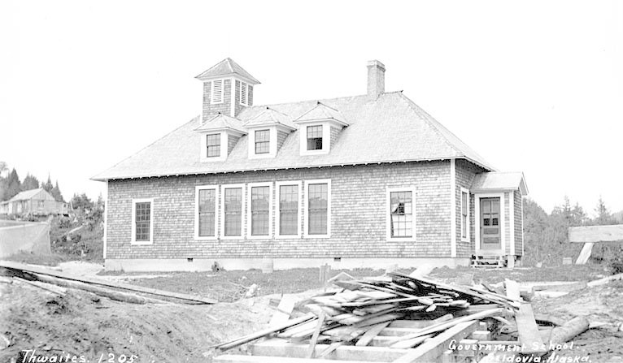 Schwarzes und weißes Foto eines Regierungsgebäudes aus dem Jahr 1905, umgeben von Bäumen unter einem klaren Himmel, mit Holzplanken und Text unten.