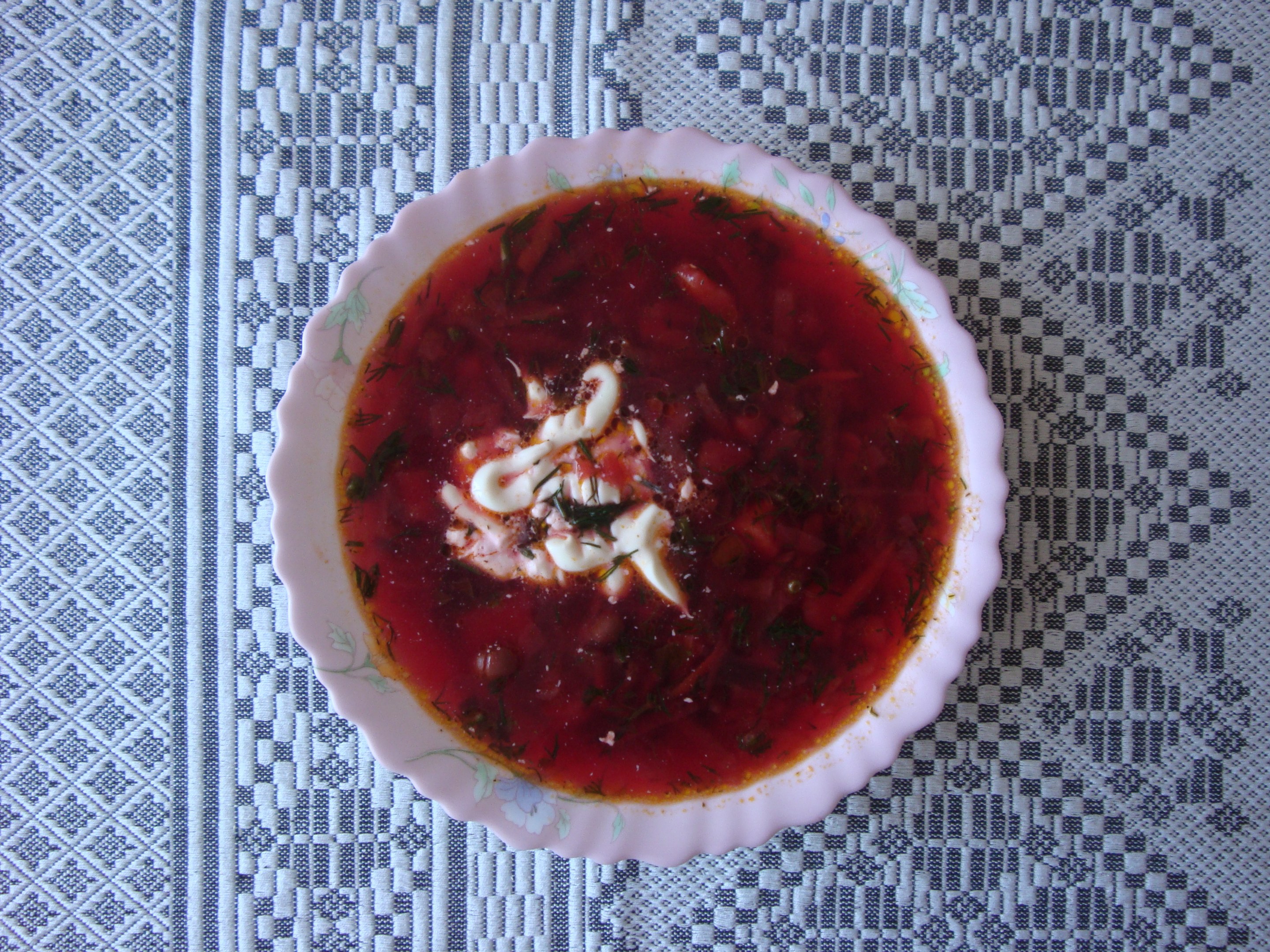 Eine tiefe rote Schüssel Borschtsch mit saurer Sahne darauf auf einem mit einem Tuch bedeckten Tisch.