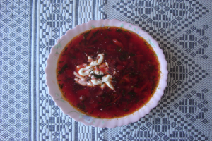 Eine tiefe rote Schüssel Borschtsch mit saurer Sahne darauf auf einem mit einem Tuch bedeckten Tisch.