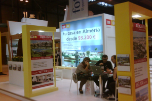 Eine Gruppe von Menschen sitzt um einen Tisch und schaut auf einen Laptop, mit mehreren Flyern, auf denen verschiedene Werbeanzeigen zu sehen sind.