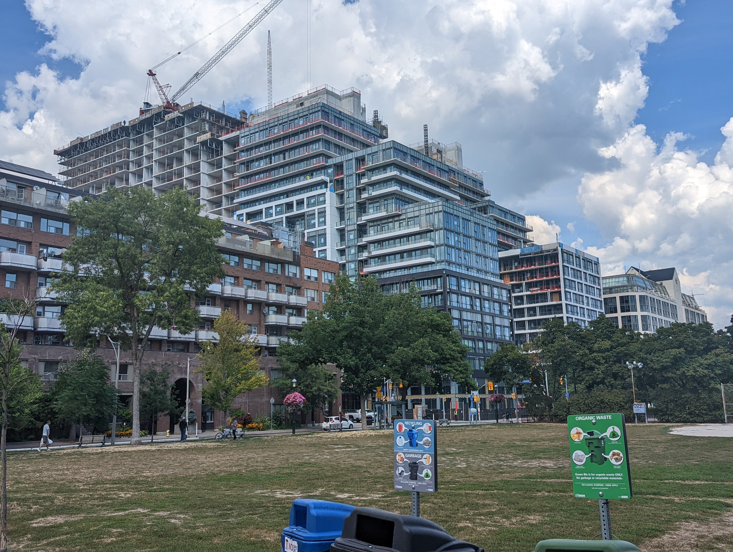 Large building under construction in a park, identified as the Toronto Housing Authority, surrounded by construction materials, trees, and people.