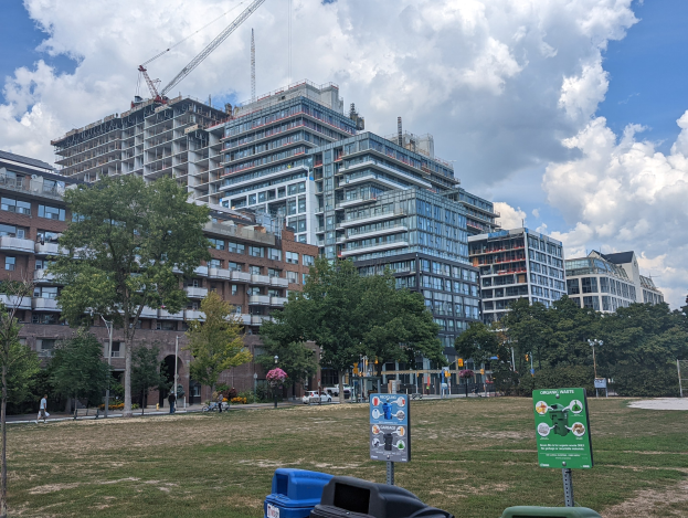 Large building under construction in a park, identified as the Toronto Housing Authority, surrounded by construction materials, trees, and people.