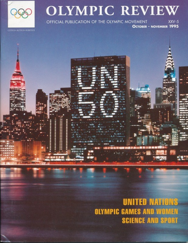 Book titled "Olympic Review Official Publication of the Olympic Movement" featuring a cityscape with buildings, lights, and water on its cover, placed on a flat surface.