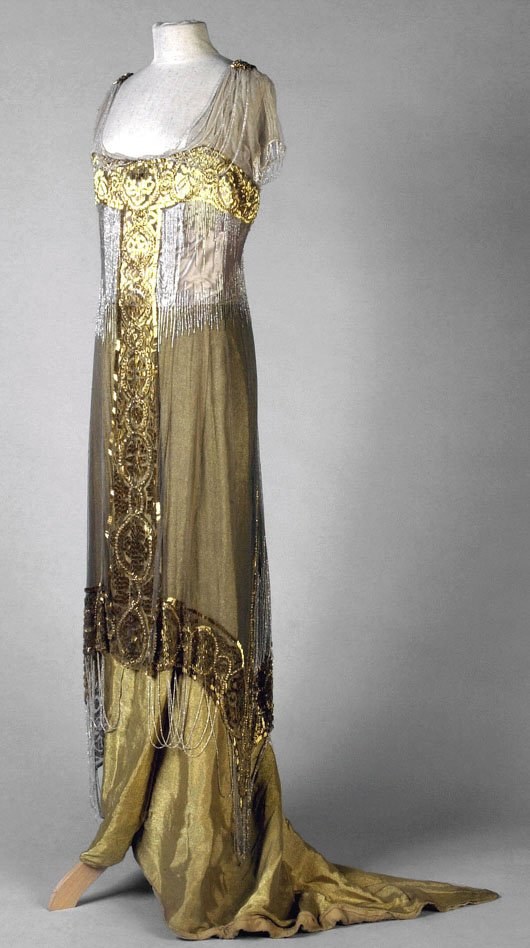 Eine Schaufensterpuppe trägt ein goldenes und silbern schimmerndes Abendkleid aus den 1920er Jahren mit aufwendiger Goldstickerei und Perlen.