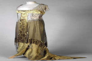 Eine Schaufensterpuppe trägt ein goldenes und silbern schimmerndes Abendkleid aus den 1920er Jahren mit aufwendiger Goldstickerei und Perlen.