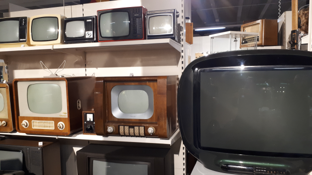 Ein Raum voller numerous alter Fernseher auf Regalen, mit einer Wand im Hintergrund und einer Decke mit Lampen oben.