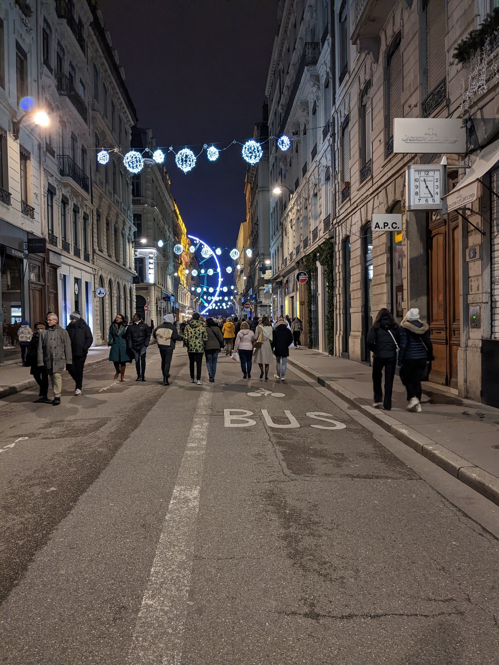 Menschen, die nachts eine Straße in Barcelona entlanggehen, beleuchtet von festlichen Weihnachtslichtern, mit Gebäuden auf beiden Seiten und dem Himmel im Hintergrund.