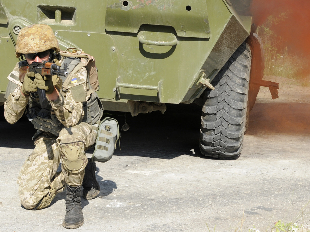 Eine Person in Kleidung, die eine Waffe mit beiden Händen hält, mit einem Fahrzeug oben im Bild.