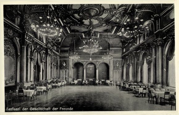Black and white photo of a large room with tables, chairs, pillars, arches, and chandeliers, labeled "Festival der Gesellschaft der Freunde, Berlin" at the bottom.