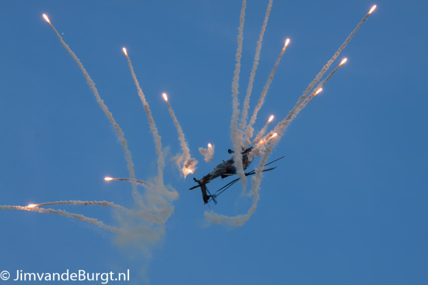 Ein Hubschrauber fliegt durch die Luft mit einer Rauchspur hinter sich, die eine Feuerspur am Himmel hinterlässt, mit Text in der linken unteren Ecke.