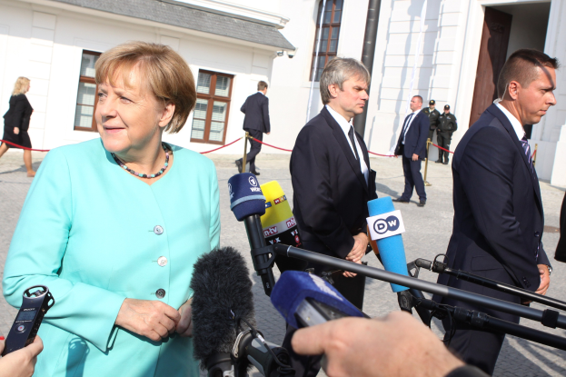 Bundeskanzlerin Angela Merkel spricht mit Reportern vor dem Kanzleramt in Berlin, umgeben von Menschen mit Mikrofonen und Geb├Ąuden im Hintergrund.