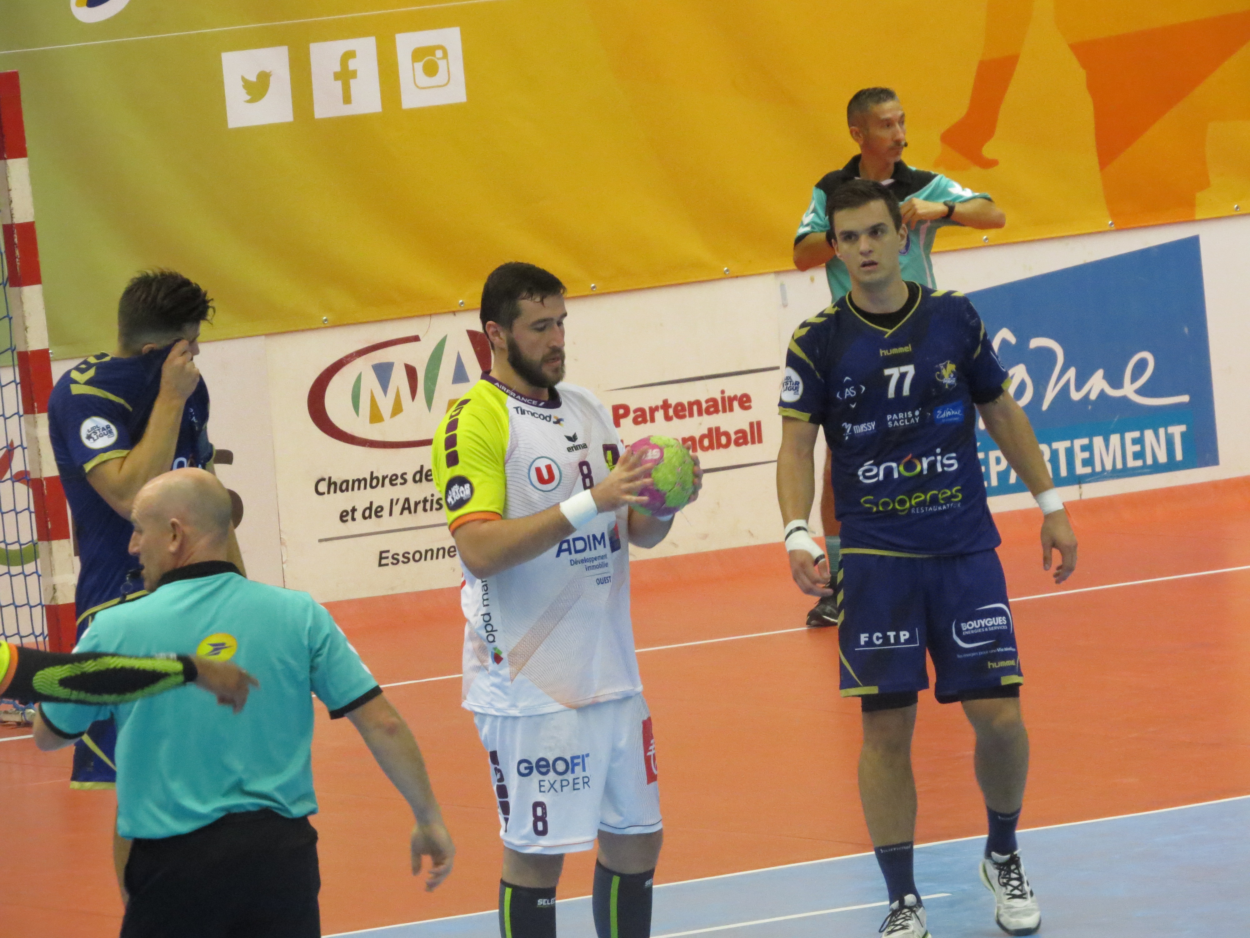 Eine Gruppe von Männern steht auf einem Futsal-Platz, einer hält einen Ball, mit einem Tor auf der linken Seite und Bannern im Hintergrund.
