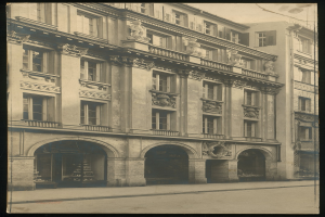 Old building with numerous windows and decorative sculptures on its facade, located along a busy city street.
