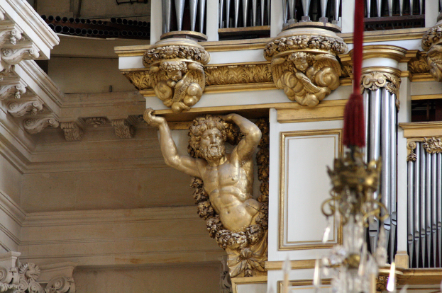 Eine Skulptur steht in der Mitte eines Raumes mit Säulen und einem Kronleuchter auf der rechten Seite.