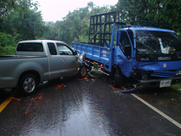 Ein geschädigter Lkw mit eingedellter Front und verbeulter Karosserie am Straßenrand, umgeben von Bäumen unter einem klaren blauen Himmel.