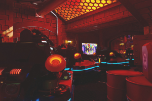 Ein hell erleuchteter Raum voller verschiedener Arcade-Videospielautomaten, Bildschirme und Gegenstände, einschließlich eines sichtbaren Rohrs und Deckenlampen.