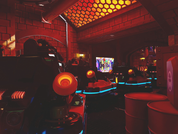 Ein hell erleuchteter Raum voller verschiedener Arcade-Videospielautomaten, Bildschirme und Gegenstände, einschließlich eines sichtbaren Rohrs und Deckenlampen.