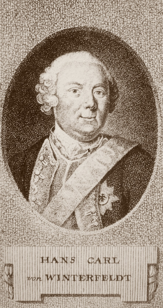 Schwarz-weiß-Foto von Hans Carl von Winterfeldt, ein Mann mit ernstem Gesichtsausdruck, mit Text unten auf dem Bild.