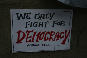 Weißer Papierbogen mit dem Text "Wir kämpfen nur für Demokratie" an einer Wand befestigt.