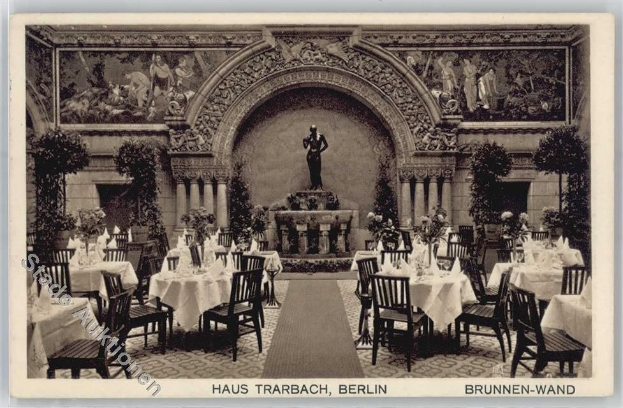 Ein altes Schwarz-Weiß-Foto eines Restaurants in Berlin, Deutschland, mit Tischen und Stühlen mit Blumenvasen, einer Statue im Hintergrund, Skulpturen und Pflanzen an den Wänden und Text unten.