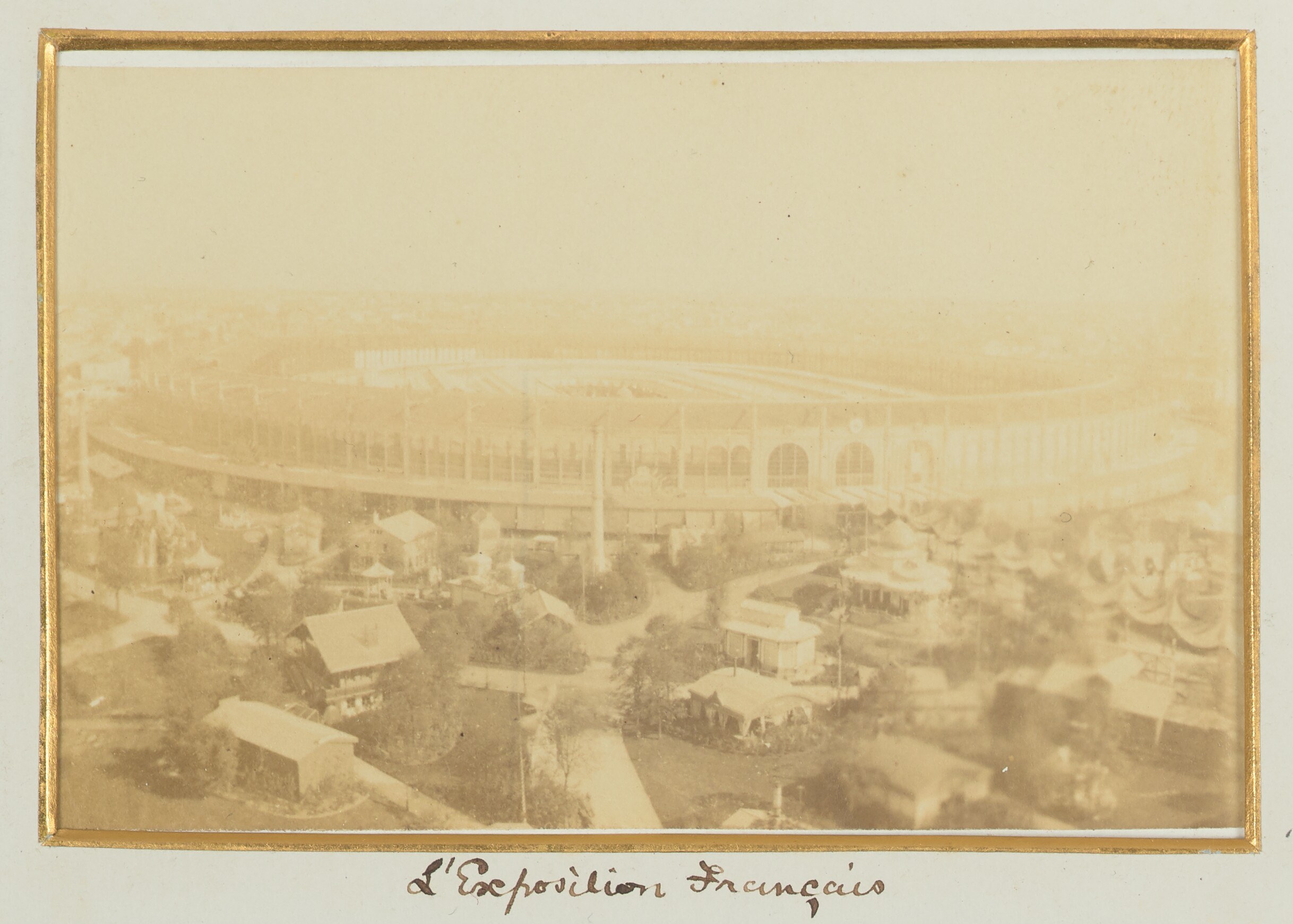 Old black-and-white photo of a stadium surrounded by city buildings, trees, and utility poles with text at the bottom.