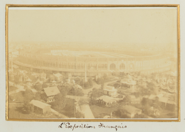 Old black-and-white photo of a stadium surrounded by city buildings, trees, and utility poles with text at the bottom.