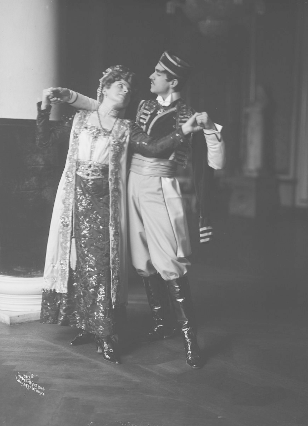 Schwarz-weiß-Foto eines Mannes und einer Frau, die in einem Ballsaal tanzen, mit einer Säule und einer Wand im Hintergrund; der Mann trägt Schuhe, was darauf hinweist, dass sie performen.