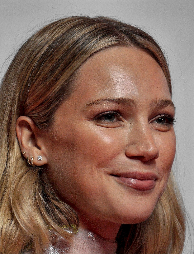 Hilary Duff strahlt mit einem schwarzen Kleid mit tiefem Ausschnitt, schwarzen High Heels und einem glatten Bob-Haarschnitt, dezent glamourösem Make-up mit rauchigem Augen-Make-up und glänzenden pinken Lippen.