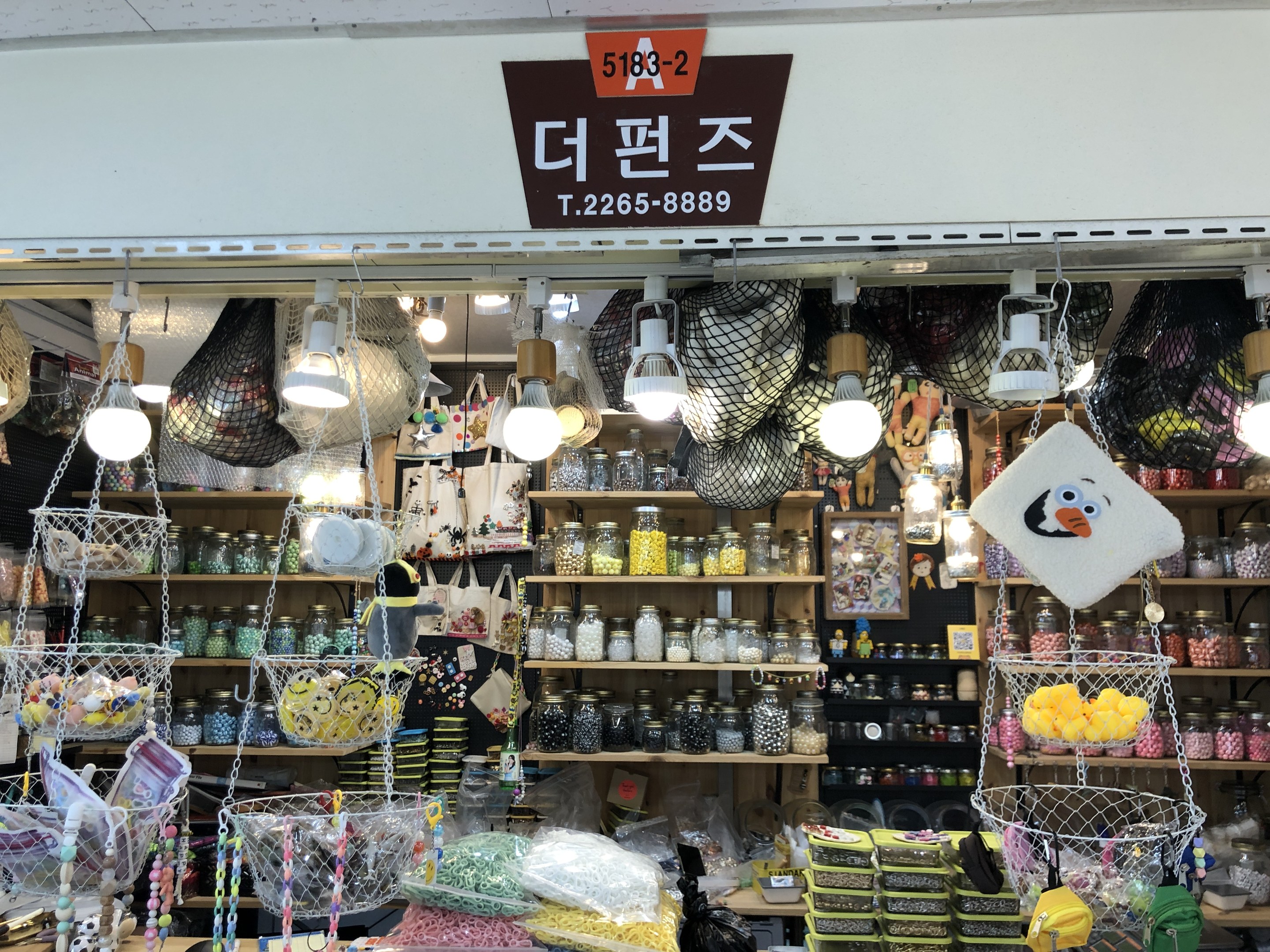 Ein Ladeneinrichtungsbild mit verschiedenen Gegenständen wie Körbchen, Lichtern, Flaschen und Spielzeugen, die auf Regalen angeordnet sind und ein Schild oben anzeigen, dass es sich um den besten koreanischen Shop in Seoul handelt.