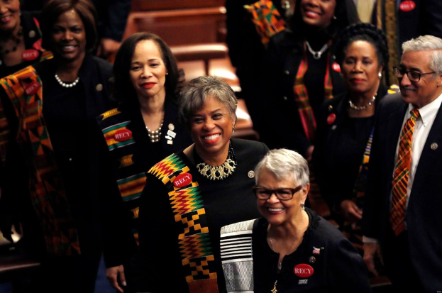 Eine Gruppe von lachenden Menschen, die zusammen in einem öffentlichen Raum stehen, wahrscheinlich wegen eines Sieges auf der Democratic National Convention, mit Bänken und einer Wand im Hintergrund.