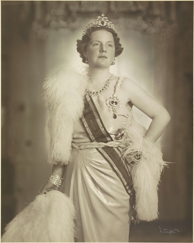 Schwarzes und weißes Foto der Queen Elizabeth II in einem Kleid und einer Krone mit einem unscharfen Hintergrund und Text unten.