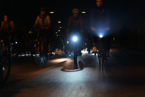 Gruppe von Menschen, die nachts mit Fahrrädern durch eine Stadtstraße fahren und alle Helme tragen.