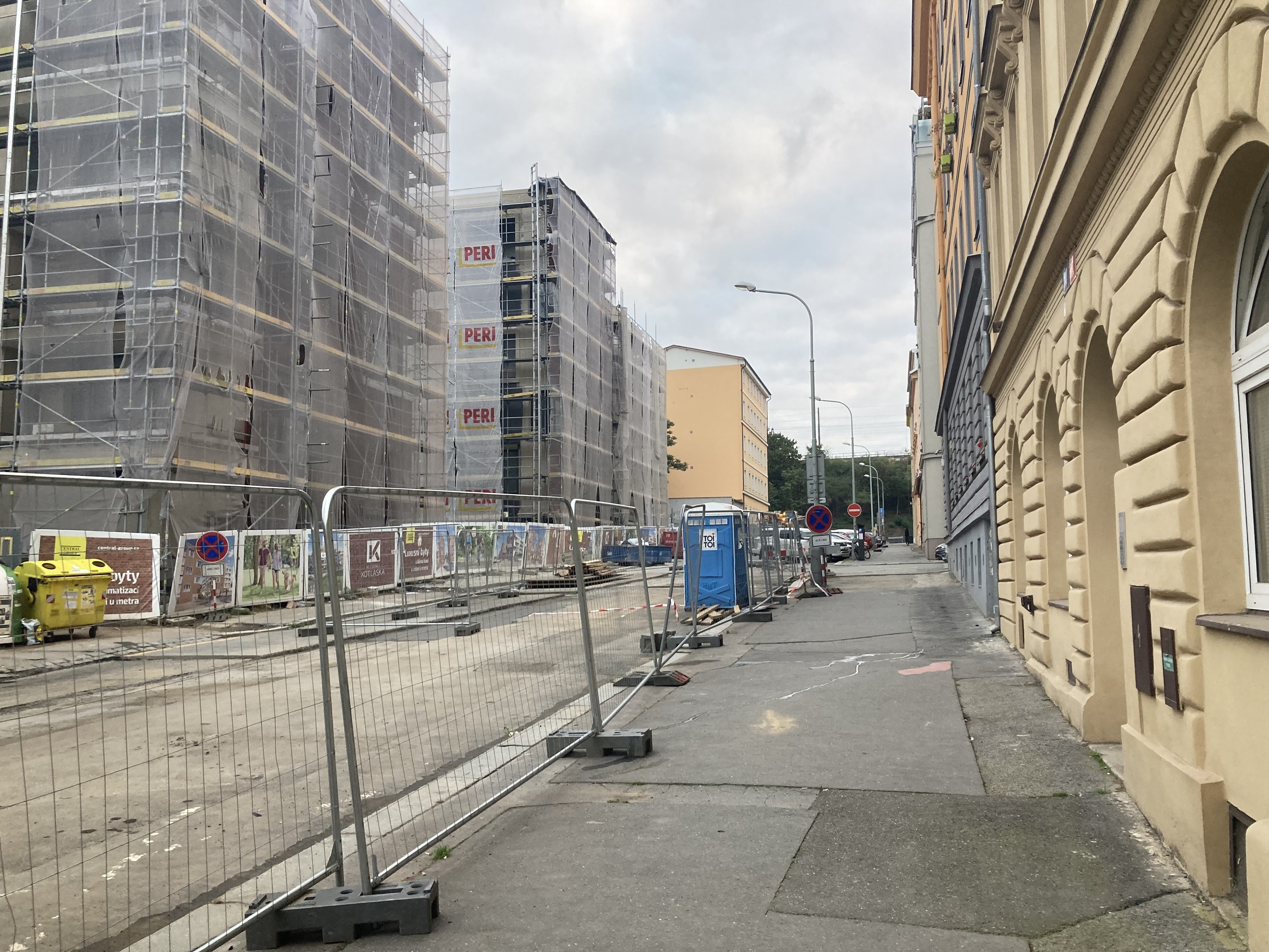 City street with buildings, vehicles, street infrastructure, trees, and a construction site with scaffolding.